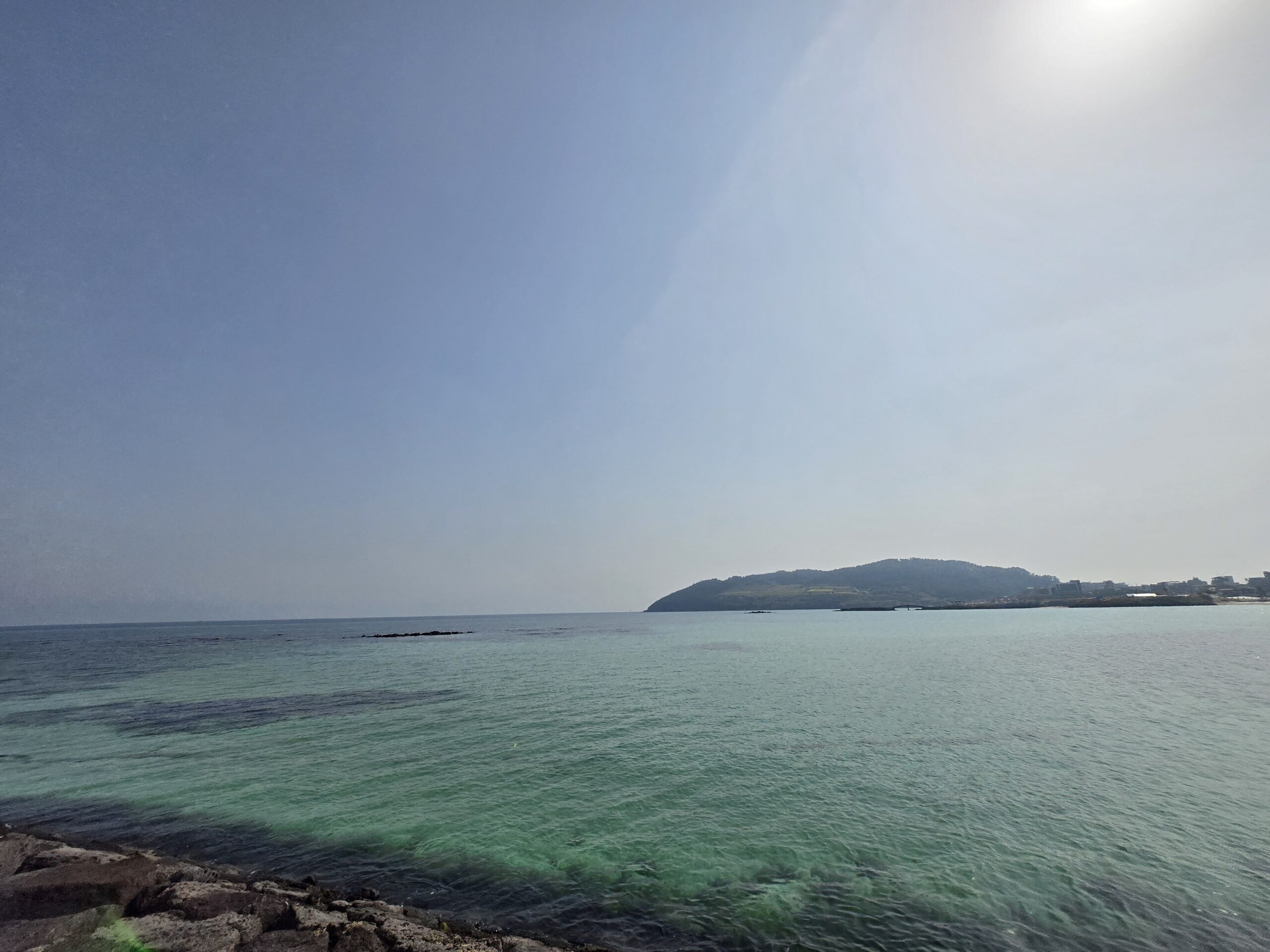 Calm sea beneath a wide hazy sky and distant shoreline